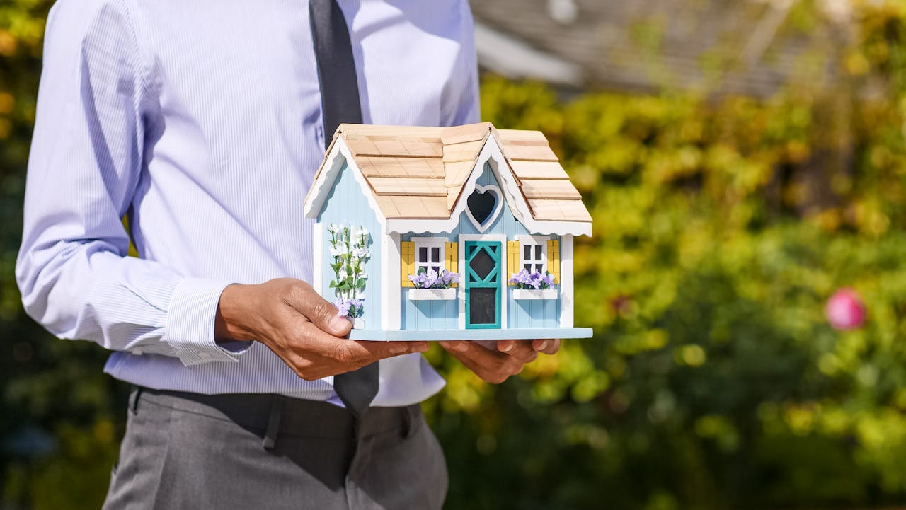 hero-img-01 Businessman holds small house model outdoors, symbolizing real estate investment.